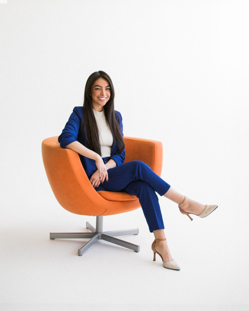 Sharissa Villanueva smiling in an orange chair with legs crossed